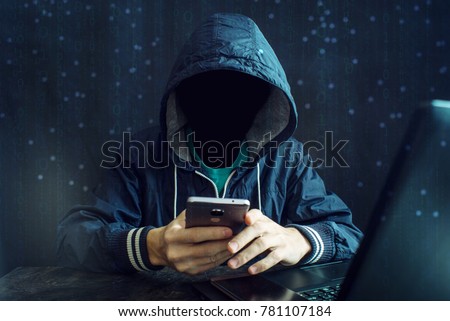 An anonymous hacker without a face uses a mobile phone to hack the system. Stealing personal data and money from Bank accounts. The concept of cyber crime and hacking electronic devices Royalty-Free Stock Photo #781107184