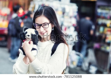 Young attractive caucasian girl with soft panda toy in her hands walking on asian street souvenir market. Travel concept. Toned image.