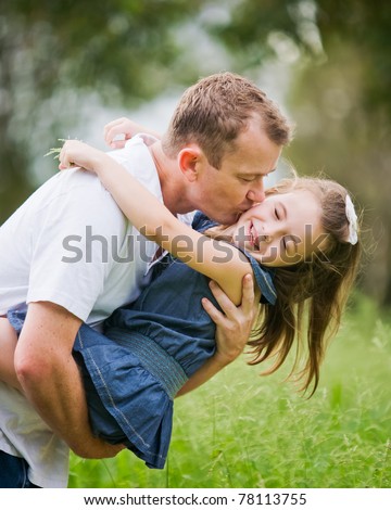 A 6 year old girl enjoying a moment of fun with her dad who is kissing her on the cheek.
