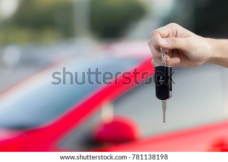 Close up hand of Man holding car key  with blurred red car on background.