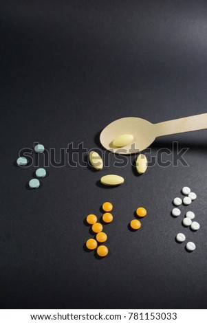 Colorful pills in wooden spoon on black paper texture background