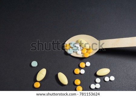 Colorful pills in wooden spoon on black paper texture background
