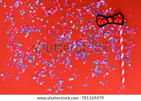 Holiday background with colorful confetti, and carnival mask paper red bow. Flat lay style. Birthday or party greeting card with copy space.