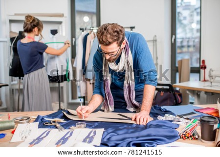 Couple of fashion designers working with fabric and clothing sketches at the studio full of tailoring tools and equipment
