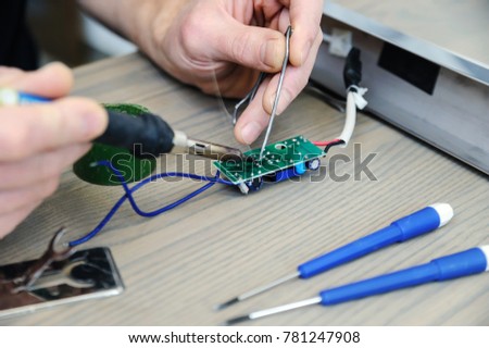 The man is repairing the power supply of the lamp. He is holding an electronic board and a soldering iron.