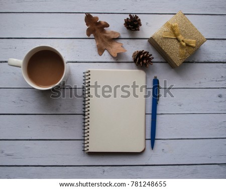  Mug of coffee, gift box, notepad, autumn leaf and cones on wooden table. 