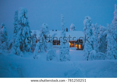 A cozy wooden cabin cottage chalet house covered in snow near ski resort in winter with the lights turn on, evening picture