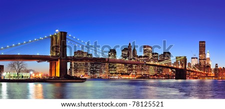 Brooklyn bridge with New York City Manhattan downtown skyline panorama at dusk illuminated over East River with blue clear sky.