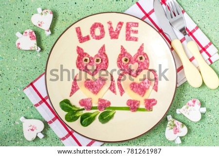 Decoration of food for Valentines Day. Appetizer of cheese and sausages. Two loving owls made up of edible hearts. Inscription love cut out of salami. Symbols of Valentines Day in design
