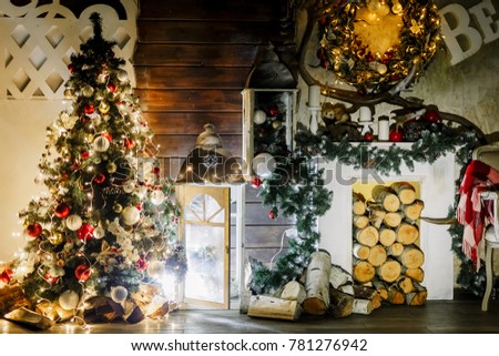 New Year 2021. Christmas beautiful lights on gold warm background. Tree, toys. Photo of interior of room with a wooden wall, wreath and garlands, fireplace with firewood. The letters from foam plastic