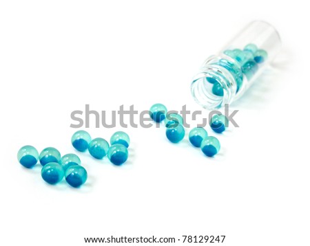 Blue pills with clear bottle spilled on a white background