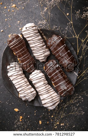 Eclairs or profiteroles with black chocolate and white chocolate with custard inside on a metal plate on a dark background. Traditional French dessert. Empty space for design text template
