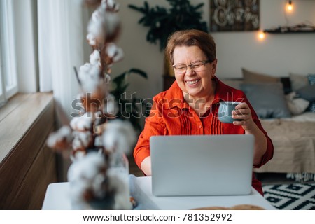 laughing Senior woman using laptop for websurfing. Mature lady with cup of coffee watching funny movie. Royalty-Free Stock Photo #781352992