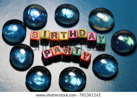 Happy Birthday party card invitation 3D words and letters spelled in blocks and beads with glass pieces on blue background.