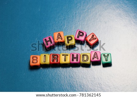 Happy Birthday party card invitation 3D words and letters spelled in blocks and beads on blue background.