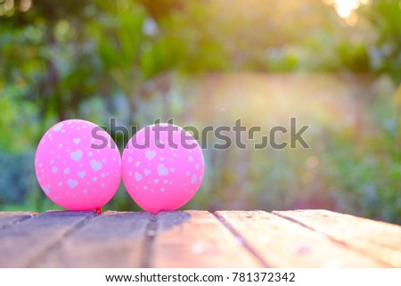 A pair of pink balloons on the old wooden table in the green garden with soft light and nature background for valentine's day concept