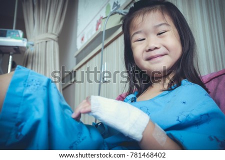 Illness asian child smiling happily and looking at camera. Young pretty girl admitted in hospital while saline intravenous (IV) on hand. Health care stories. Vintage film filter effect.