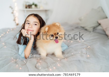 Child girl is holding puppy on her hands on the bed in her decorated bedroom