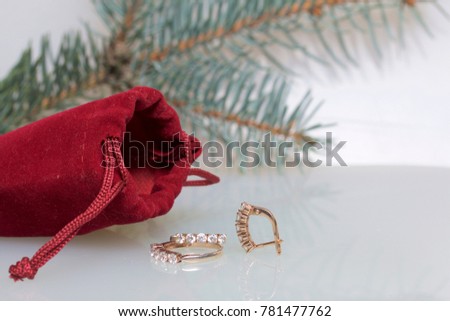 A gift to a loved one. A velvet red pouch. Nearby is a golden ring and gold earrings. On a white background with a spruce branch.