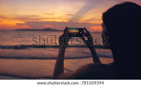 Closeup of young tourist woman photographs ocean view with smartphone during sunset at beach