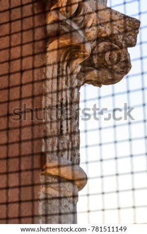 Ferrara, Italy. On top of the cathedral bell tower, detail of the richly decarated capital of the stone columns of this renaissance structure seen through the security metal grid