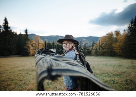 Young blonde girl in a hat, poncho and glasses running in the mountains. Autumn picture. Lifestyle.