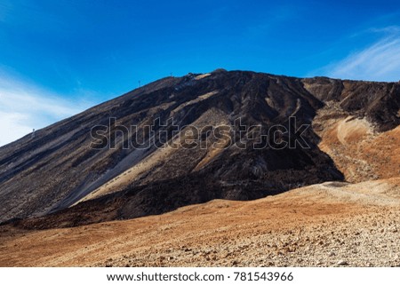 An uphill view of the colourful Teide volcano in Teide National Park, Tenerife, Canary Islands. Pictured in the distance is a cablecar leading up to the 3718 m Teide peak, the tallest peak in Spain.