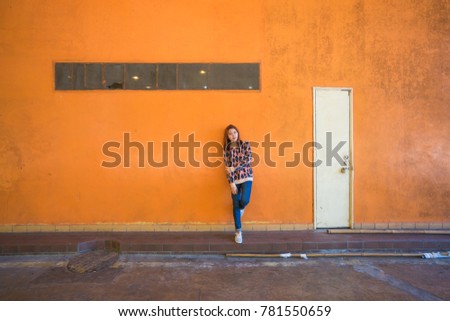 Young beautiful urban girl leans against a orange concrete wall