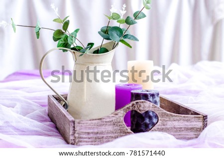 Decor in trendy colors, ultra violet, candles and vase with green leaves on a wooden tray on the background of white curtains.  Royalty-Free Stock Photo #781571440