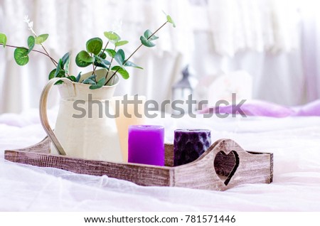 Decor in trendy colors, ultra violet, candles and vase with green leaves on a wooden tray on the background of white curtains.  Royalty-Free Stock Photo #781571446