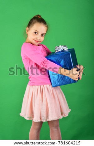 Child with smiling face poses with present on green background. Girl with wrapped gift box for holiday. New Year presents concept. Lady hugs blue gift for Christmas.