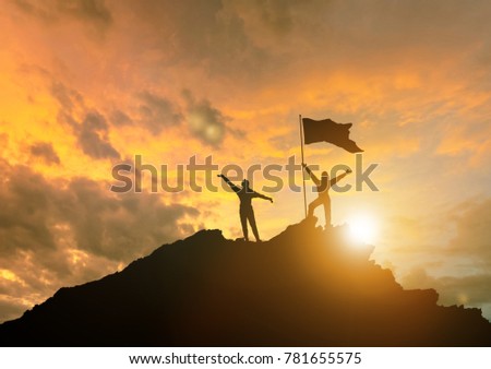 The conquest of the summit, the silhouettes of two people on top of the mountain, with their hands up.  Against the sky with clouds at sunset. Royalty-Free Stock Photo #781655575