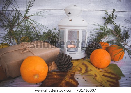 Candlestick with a burning candle, on a wooden table decorated with a Christmas tree, New Year's toys for a Christmas tree, mandarins and cones, creates a New Year mood
