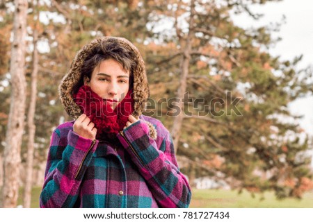 Cute brunette girl standing in park, wearing coat and scarf. Winter fashion concept.