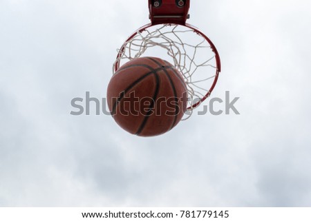 Ball inside red basketball hoop, basket against white sky. Outdoor basketball court. 
