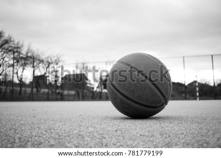 Black and white image of used orange leather basketball on grey asphalt background. 