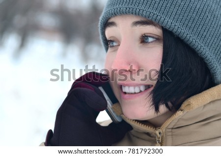 Portrait of pretty attractive caucasian pierced girl hipster in winter park. She is talking on modern smartphone. Youth street fashion. Winter fun. Walks in the open air.