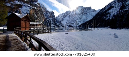 sun setting, with a beautiful reflection, behind the lake of Braies framed by the snow-capped mountains and the blue sky