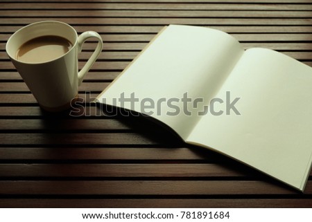 Top view a white cup of coffee is on the wooden table and this picture has blank pages of notebook, space for copy or text. Warming Sunshine  in the morning