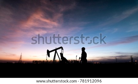 Silhouette of oilfield worker at  crude oil pump in the oilfield at sunset. Royalty-Free Stock Photo #781912096