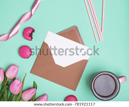 Envelope with blank paper, pink tulips, coffee and macarons, top view. Spring concept.