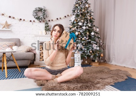 the girl sits next to a tree and a fireplace and opens Christmas presents and tries to guess what is there