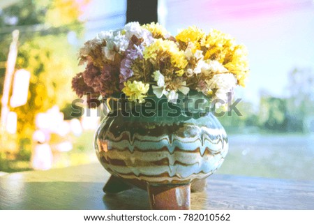 The soft focus of a beautiful flower vase is placed on a wooden table in a coffee shop with a glass. The atmosphere outside the shop is orange-yellow in winter. Chiang Mai Thailand