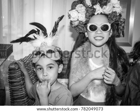 Birthday party: black and white image of a young boy wearing a mask and a young girl wearing a flower crown and sunglasses 