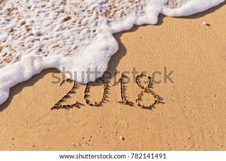 Inscription Number 2018 handwritten on seashore sand and foamy wave. New beginnings and expectations concept