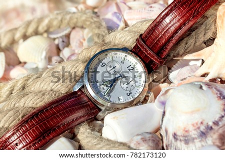 men's watches lie on seashells by the sea