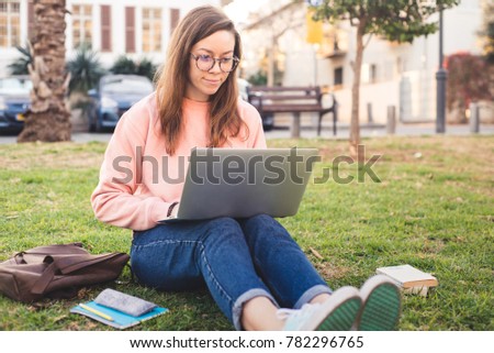 A young student girl with a laptop typing. Wearing glasses and looking into the screen
