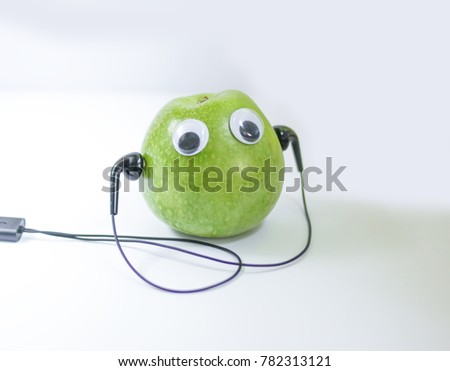Green small apple with cute eyes and headphones on white background. Conceptual photo.