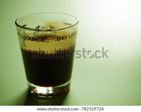 One fluid ounce of rich black coffee or espresso in shot glass on pastel green background with beautiful sunspot. (close up, selective focus, toned, space for text)