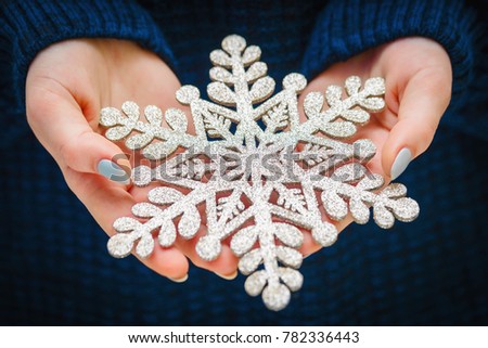 Closeup girl hands with New Year's manicure holds shining, verdant artificial snowflakes with glitter. element of Christmas decorations. snowflake is symbol of winter holiday.